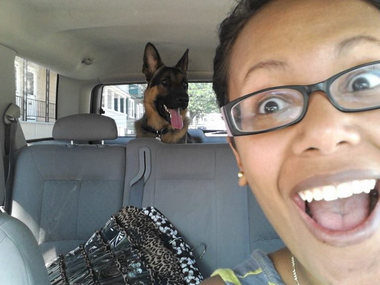 A smiling, excited Vanessa Rosa taking a selfie in her 2006 Saturn Vue, with her German Shepherd sitting in the back cargo area