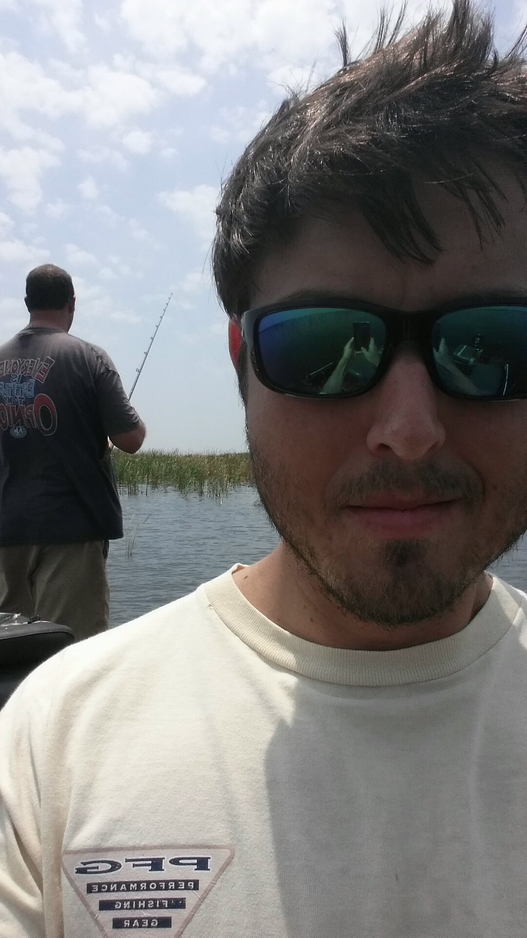 Linc Thomas smiling in reflective sunglasses with a friend fishing in the background