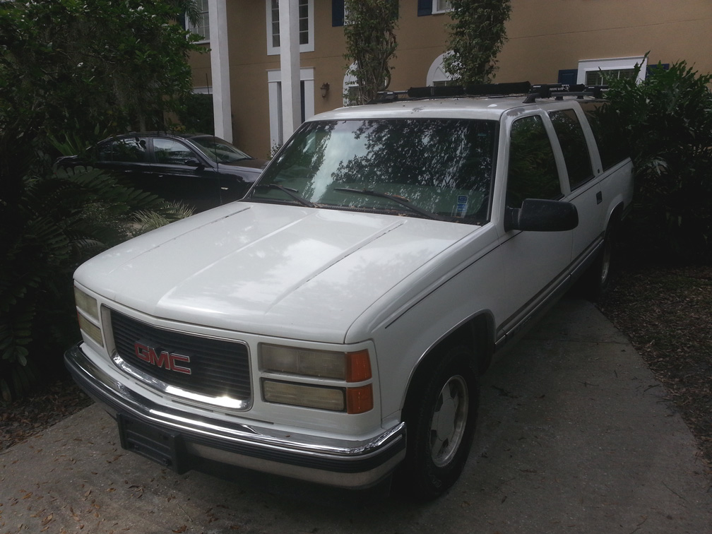Dale Novak's white 1999 Suburban SUV with a roof rack, parked on a concrete driveway