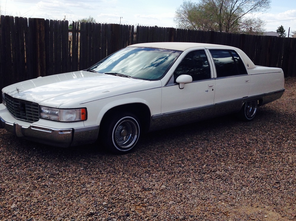 Jeffrey Aragon's white 1993 Cadillac Fleetwood sedan with wire-spoke wheels, parked on a gravel lot