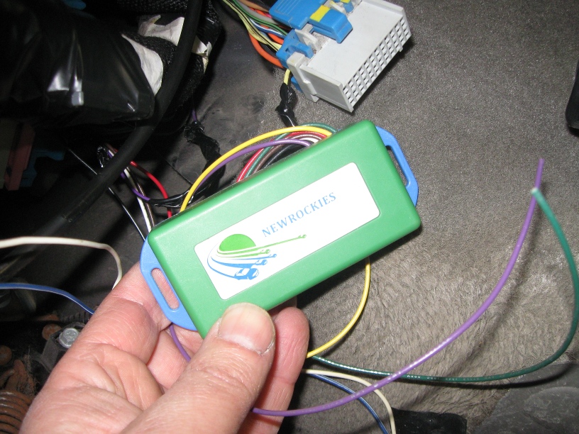 A hand holding the NEWROCKIES PRO Module with its wiring harness before installation