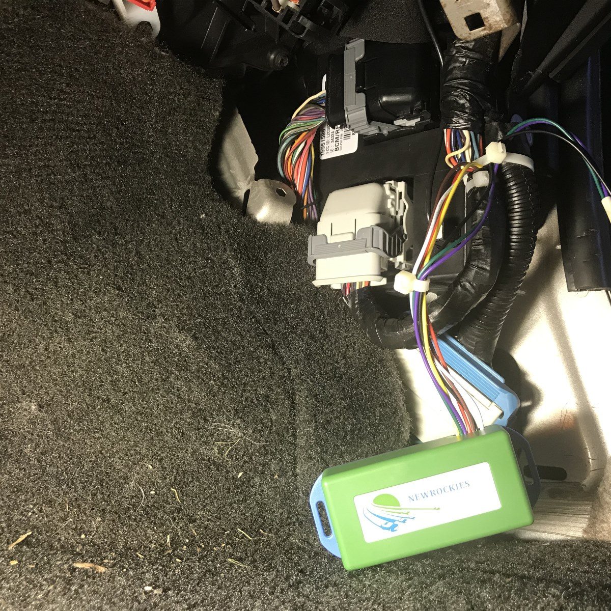 Green NEWROCKIES module connected to the Hummer H3 wiring harness near the floor carpet
