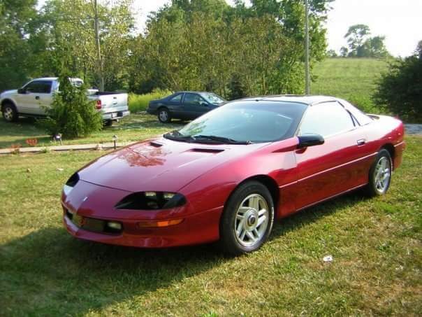 The red Camaro with a white pickup and a dark sedan behind it