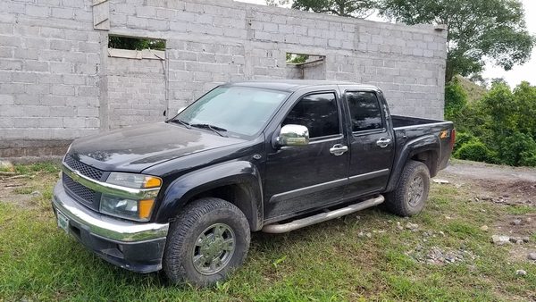 Black Chevrolet Colorado parked on grass in front of an unfinished cinder block building in Honduras